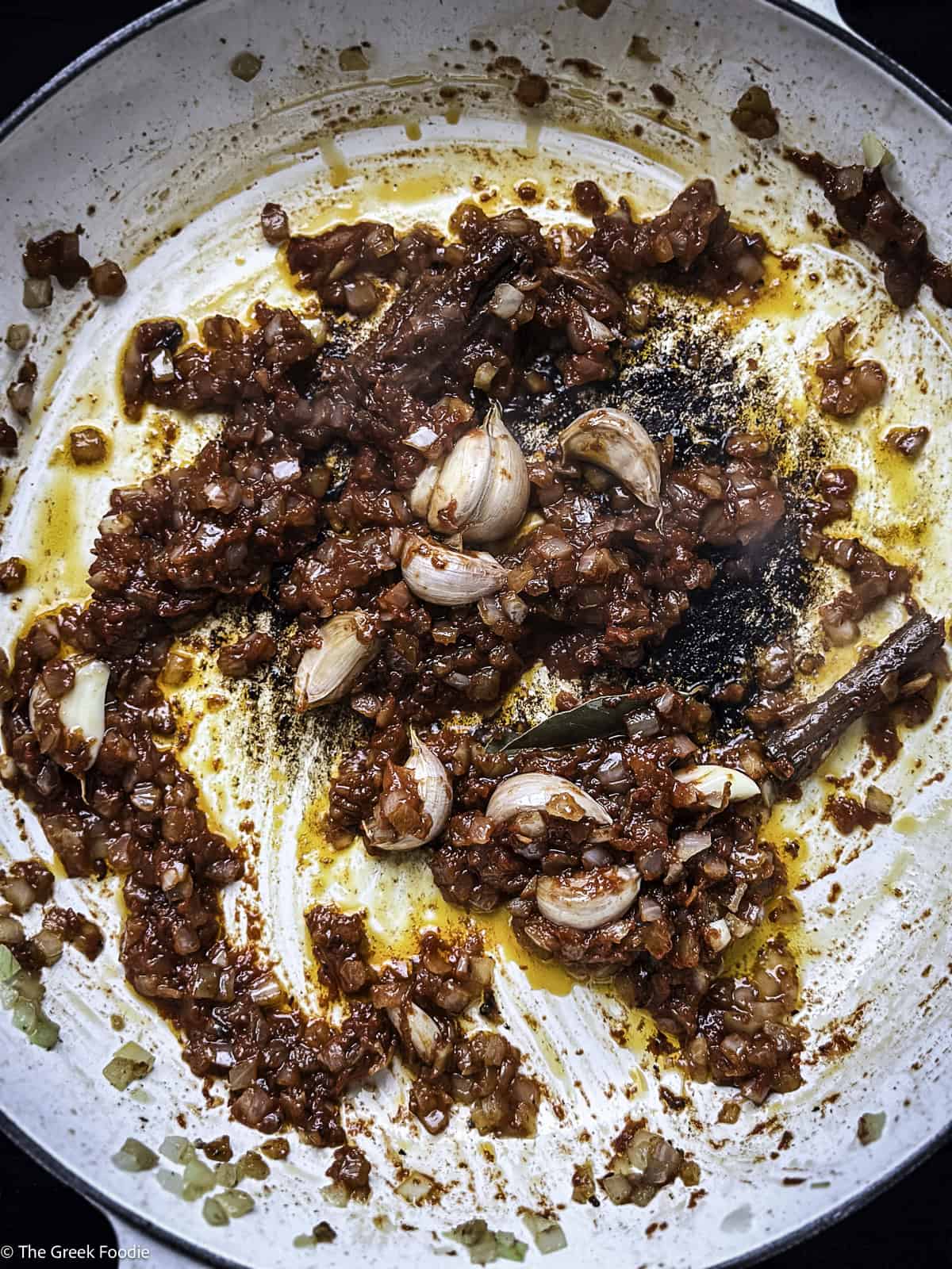Diced onion, garlic and tomato paste cooking in a white skillet.
