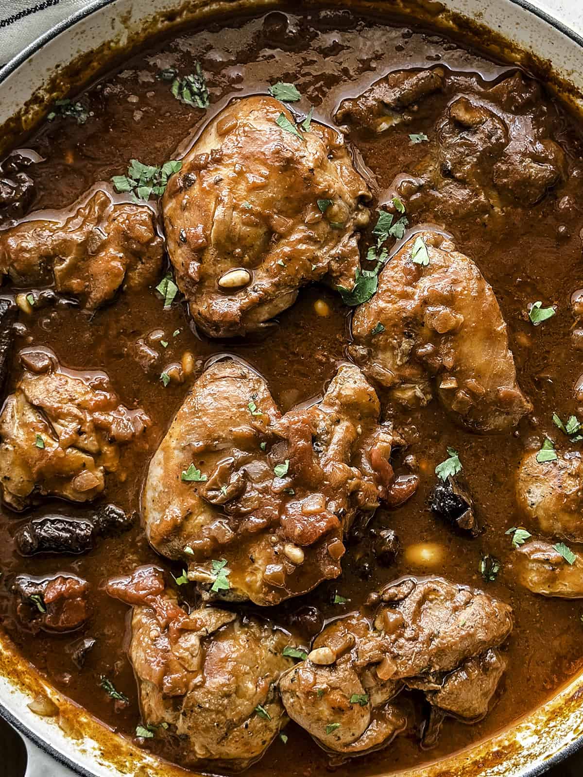 A white skillet with Greek chicken stew on a table with a loaf of bread and a pepper mill.