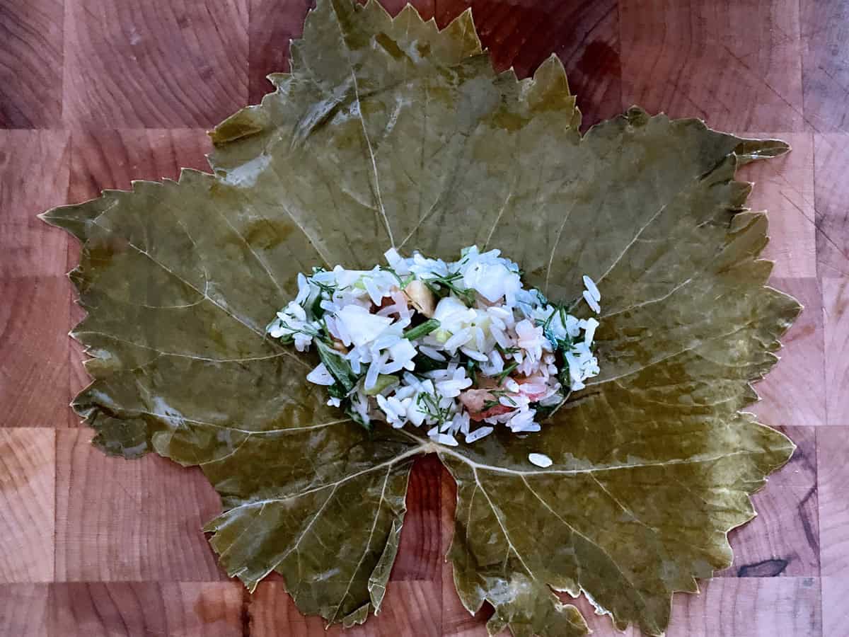 Dolmadakia rice mixture in the center of a grape leaf on a wooden surface.
