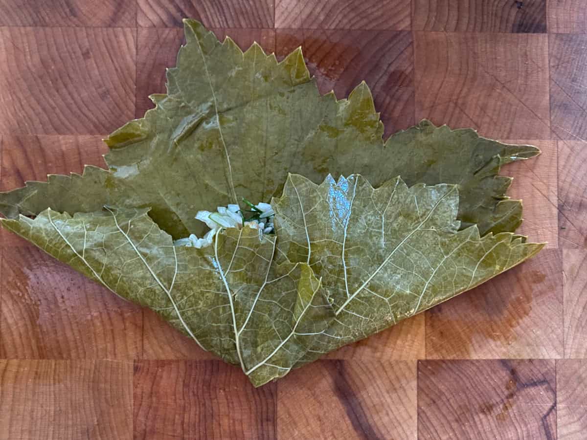 A half-folded dolmadaki-stuffed grape leaf on a wooden board.