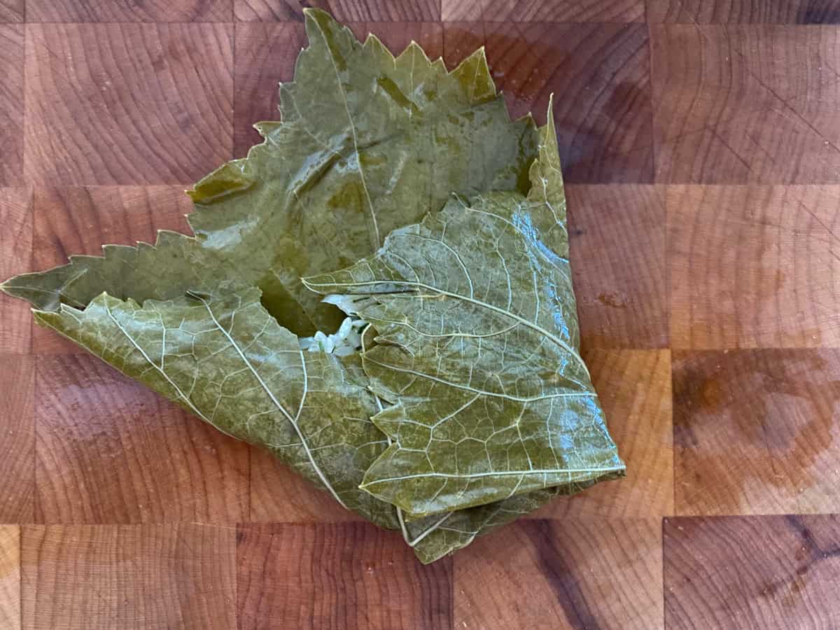A half-folded dolmadaki-stuffed grape leaf on a wooden board.