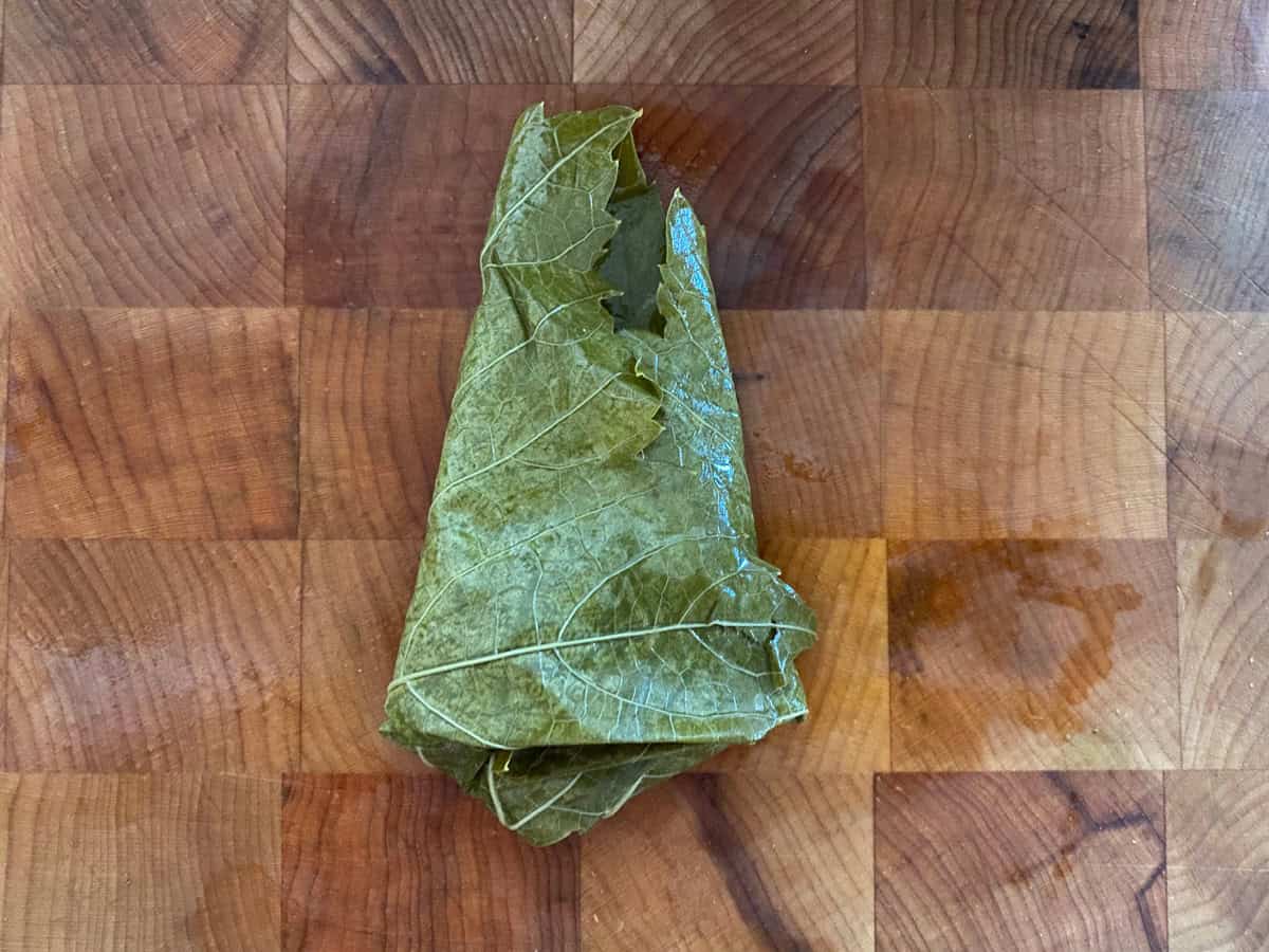 A half-folded dolmadaki-stuffed grape leaf on a wooden board.