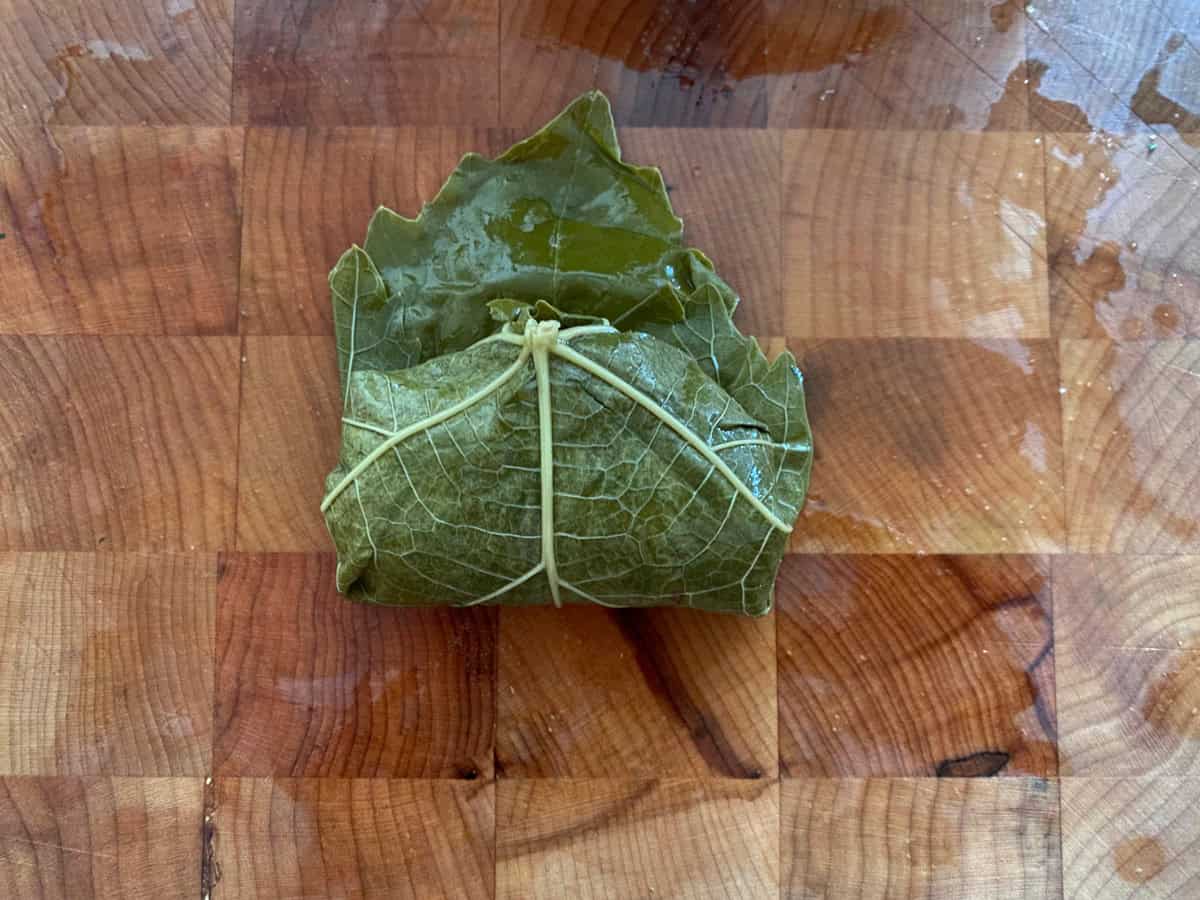 A folded dolmadaki-stuffed grape leaf on a wooden board.