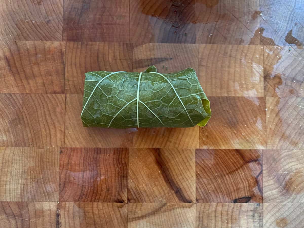 A folded dolmadaki-stuffed grape leaf on a wooden board.