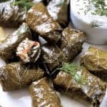 A plate with Greek dolmadakia-stuffed grape leaves and a small container with yogurt sauce.