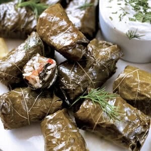 A plate with Greek dolmadakia-stuffed grape leaves and a small container with yogurt sauce.