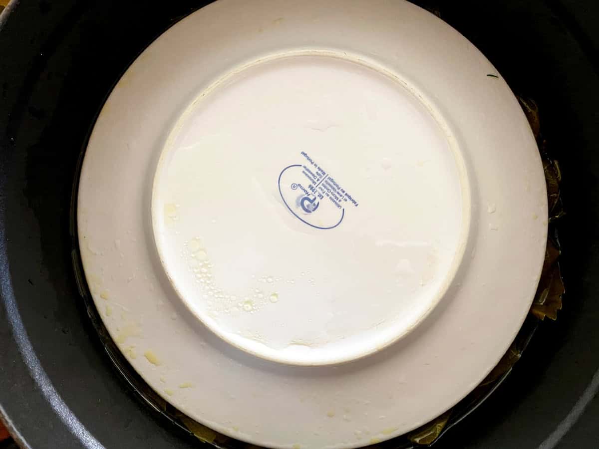 A plate upside-down covering dolmadakia in a pot.