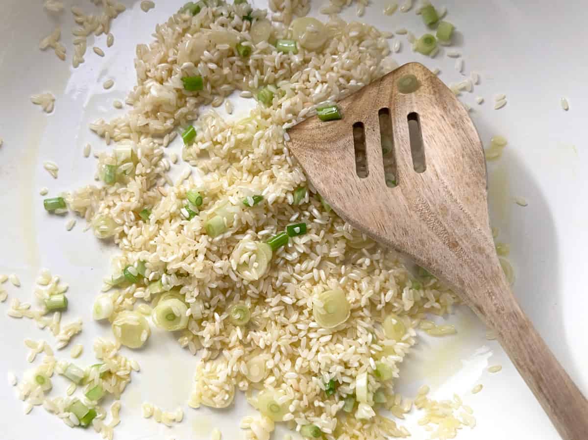 Spring onions, rice and a wooden spoon in a sauce pan.