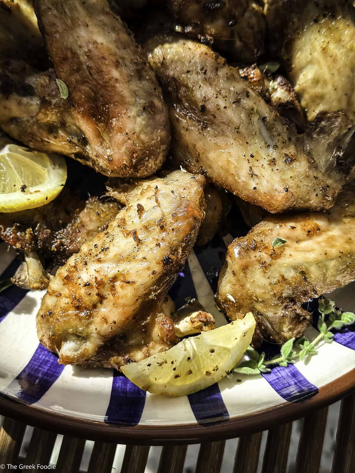 Lemon pepper chicken wings in a bowl with lemon slices.