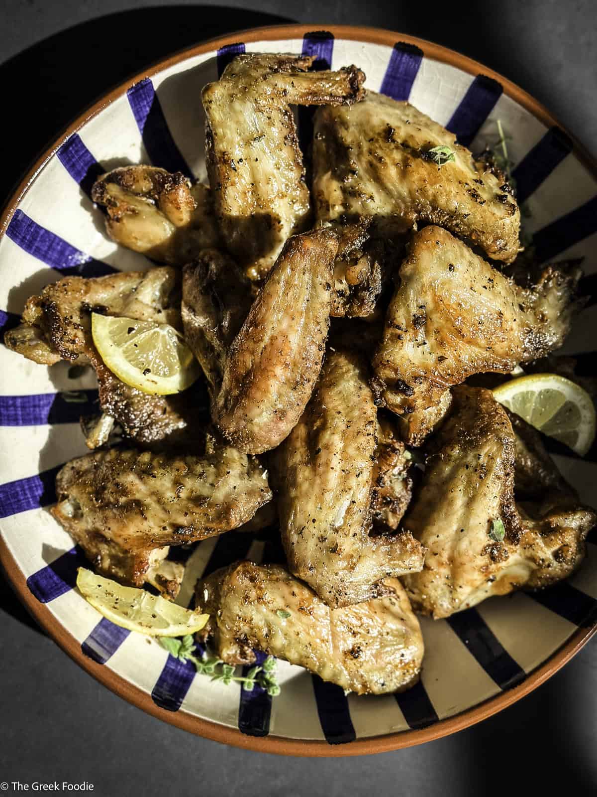 Lemon pepper chicken wings in a bowl with lemon slices.