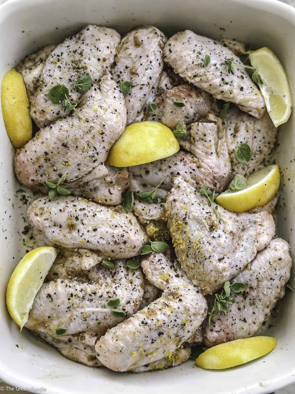 Chicken wings marinating in lemon pepper seasonings with lemon wedges.
