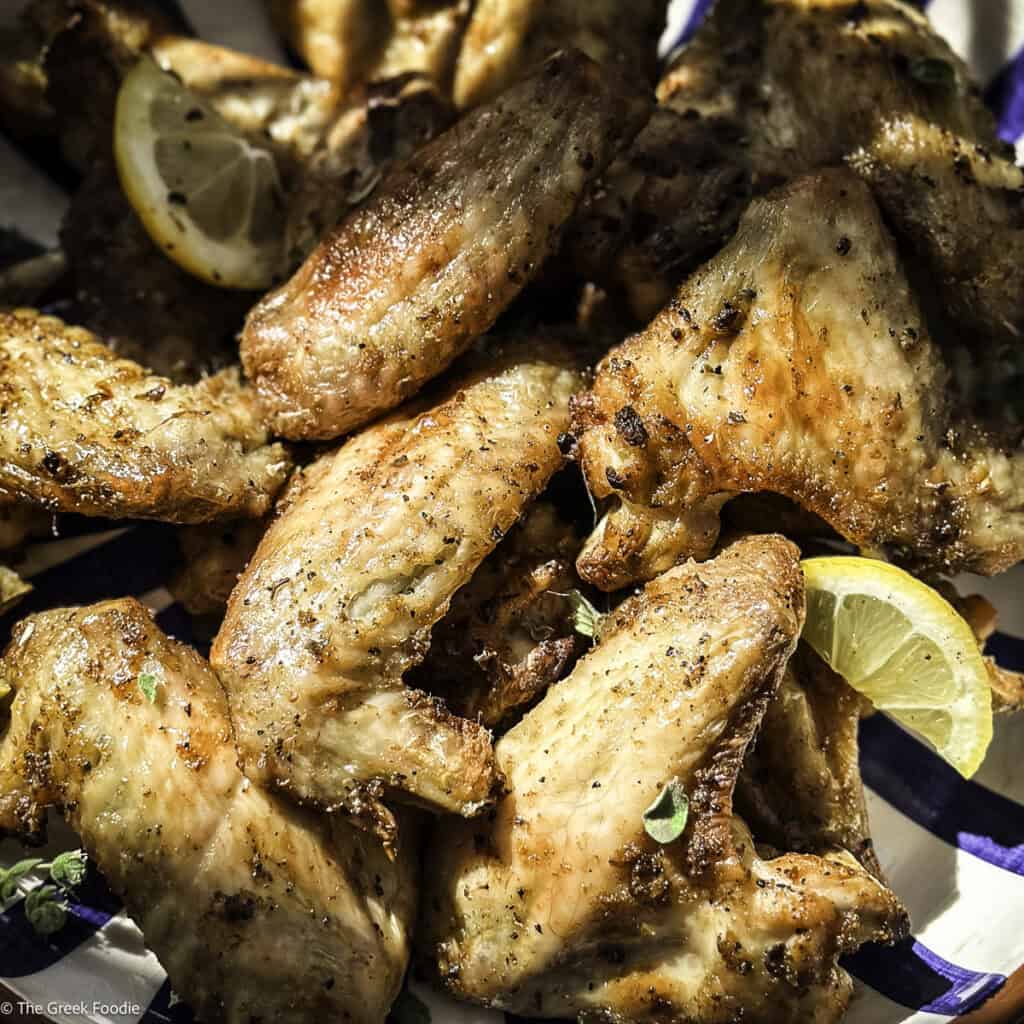 Lemon pepper chicken wings in a bowl with lemon slices.