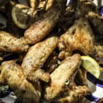 Lemon pepper chicken wings in a bowl with lemon slices.