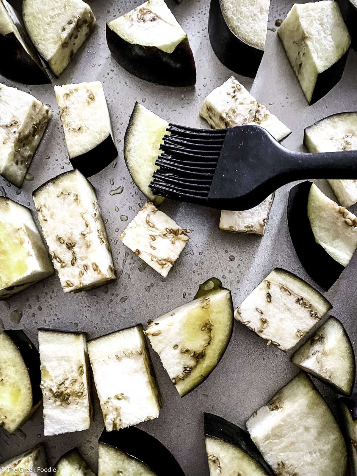 Brushing olive oil on eggplant cubes.