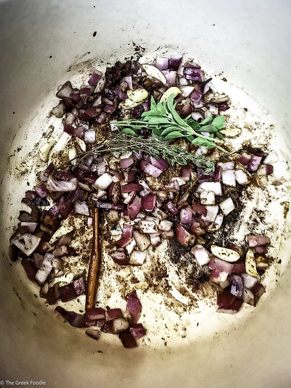 Diced onion, herbs and a cinnamon stick browning in a pot.