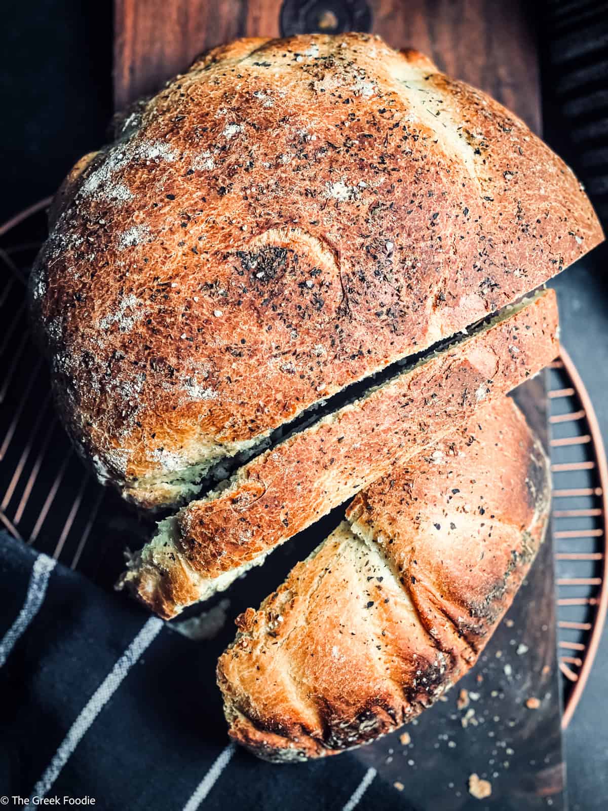 A loaf of Greek bread with two slices cut on a wooden cutting board. A metal coaster under it.