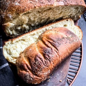 A loaf of Greek bread with two slices cut on a wooden cutting board. A metal coaster under it.