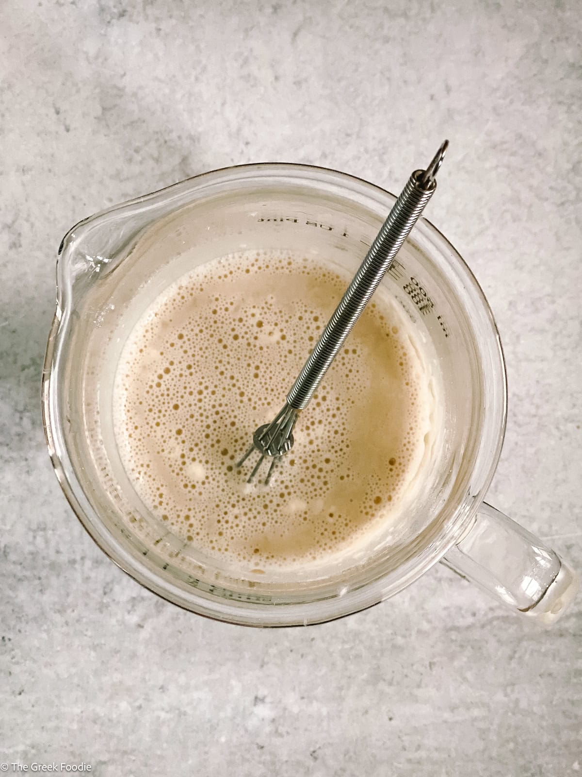 A glass measuring cup with water yeast and a stirring spoon.