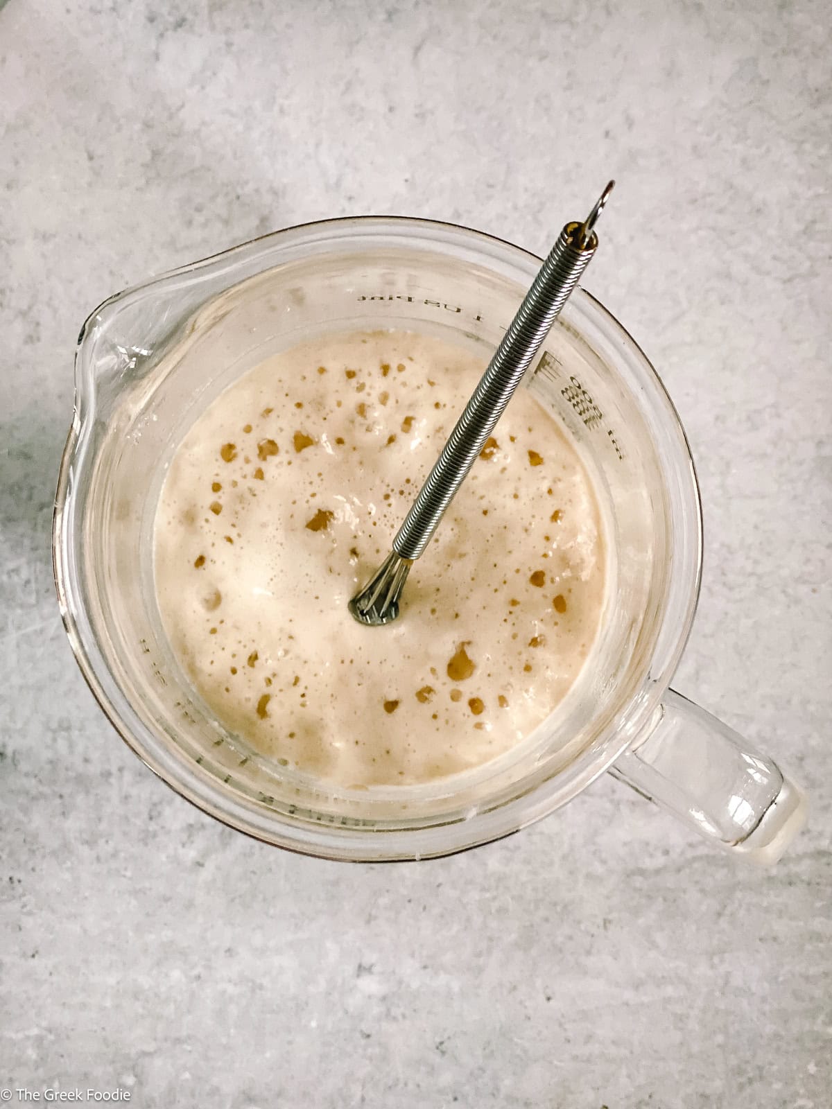 A glass measuring cup with water yeast and a stirring spoon.