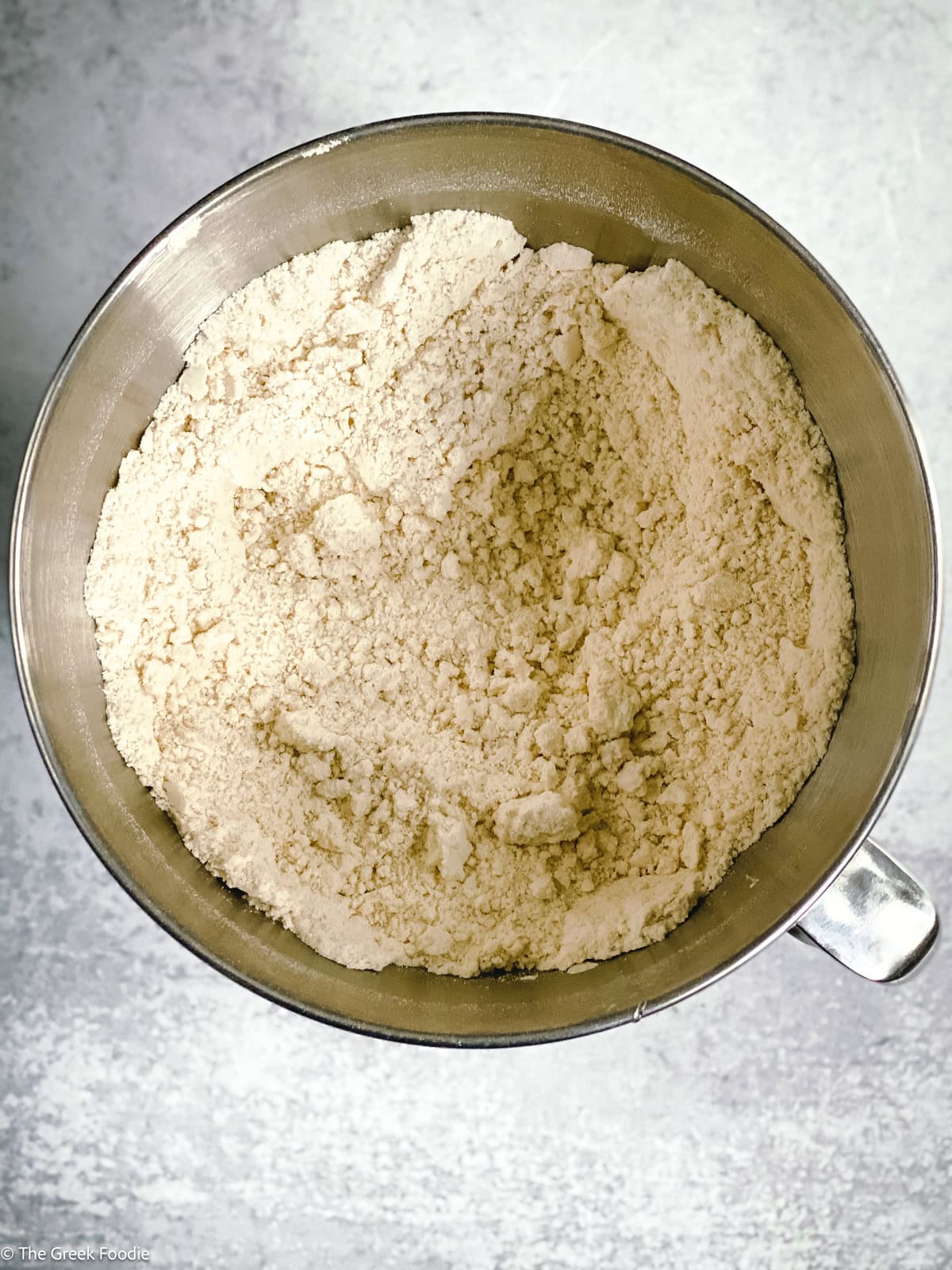 A metallic bowl with flour on a cement surface.