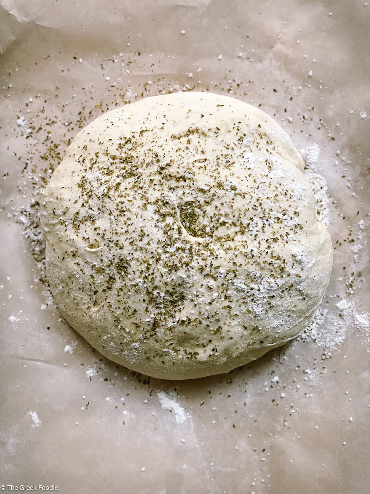 Bread dough on parchment paper with dried oregano on top.