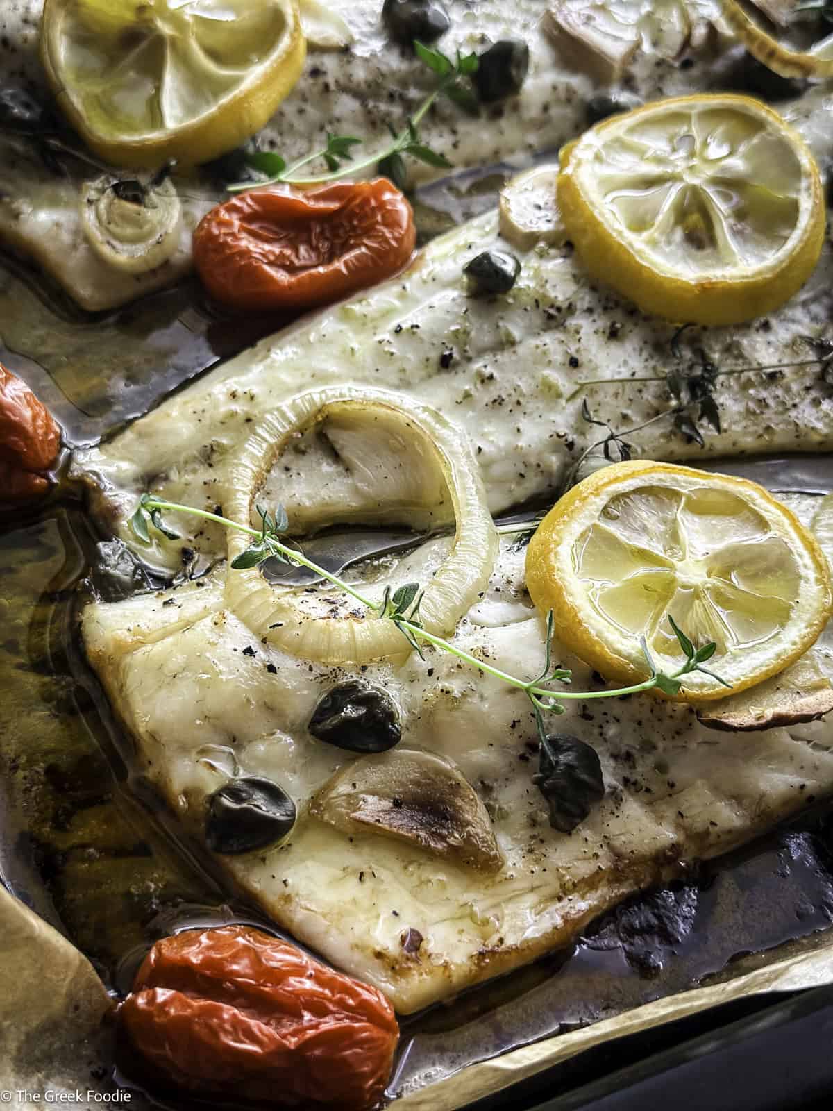 Roasted branzino fillets with cherry tomatoes and lemon slices in a baking tray.
