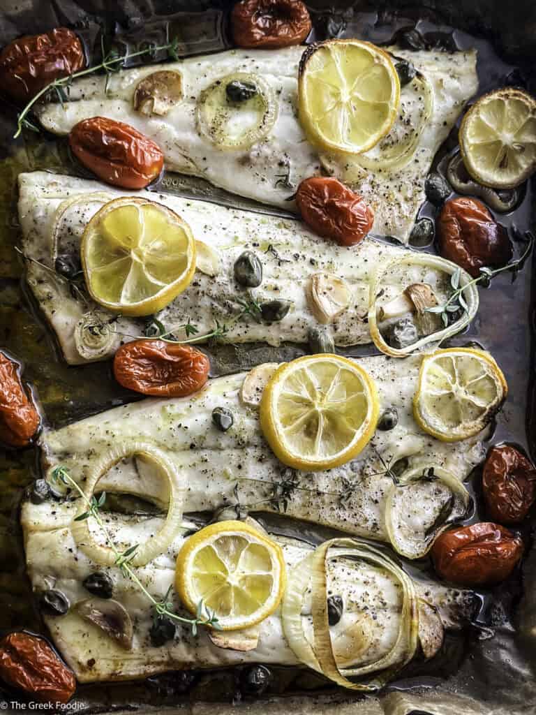 Roasted branzino fillets with cherry tomatoes and lemon slices in a baking tray.