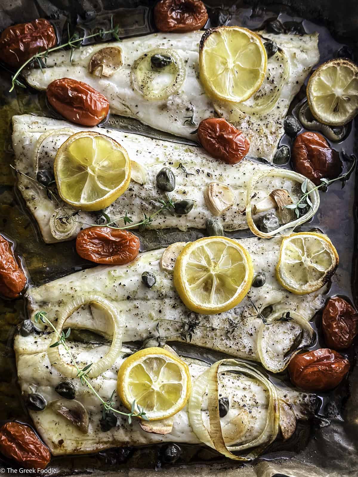 Roasted branzino fillets with cherry tomatoes and lemon slices in a baking tray.