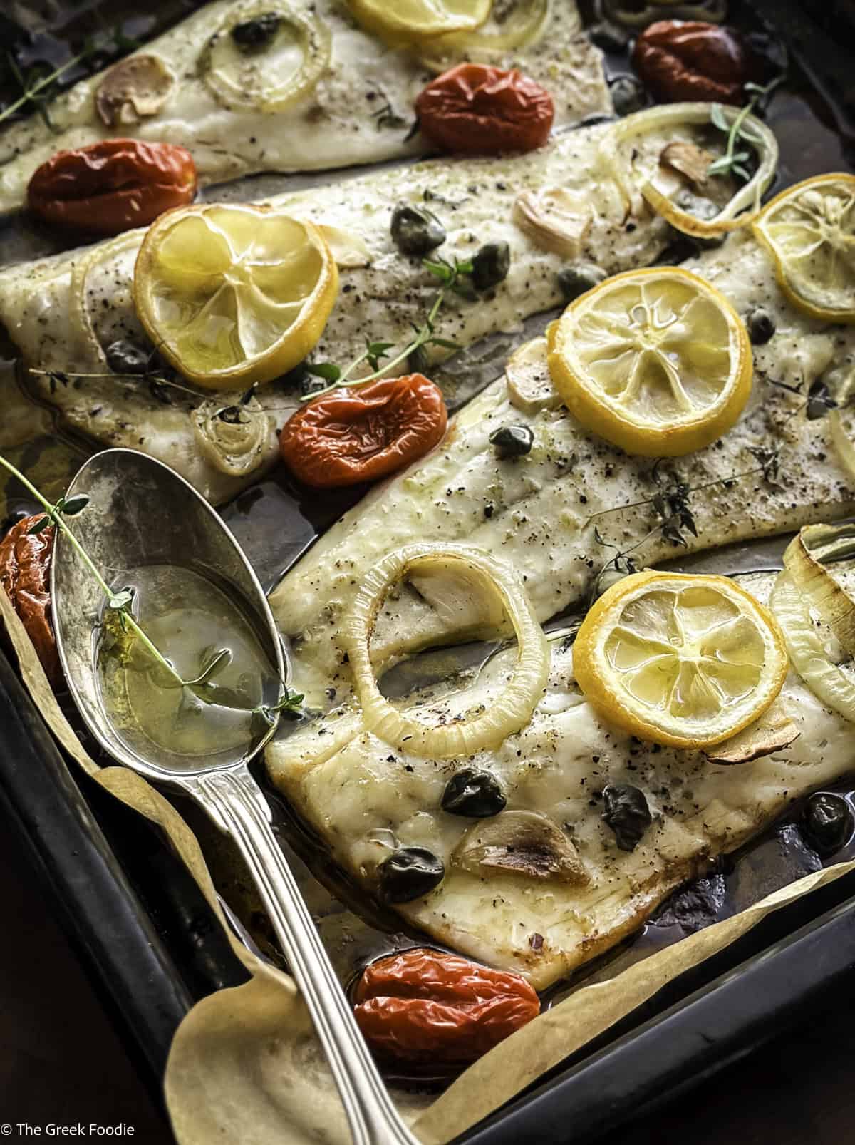 Roasted branzino fillets with cherry tomatoes and lemon slices in a baking tray.