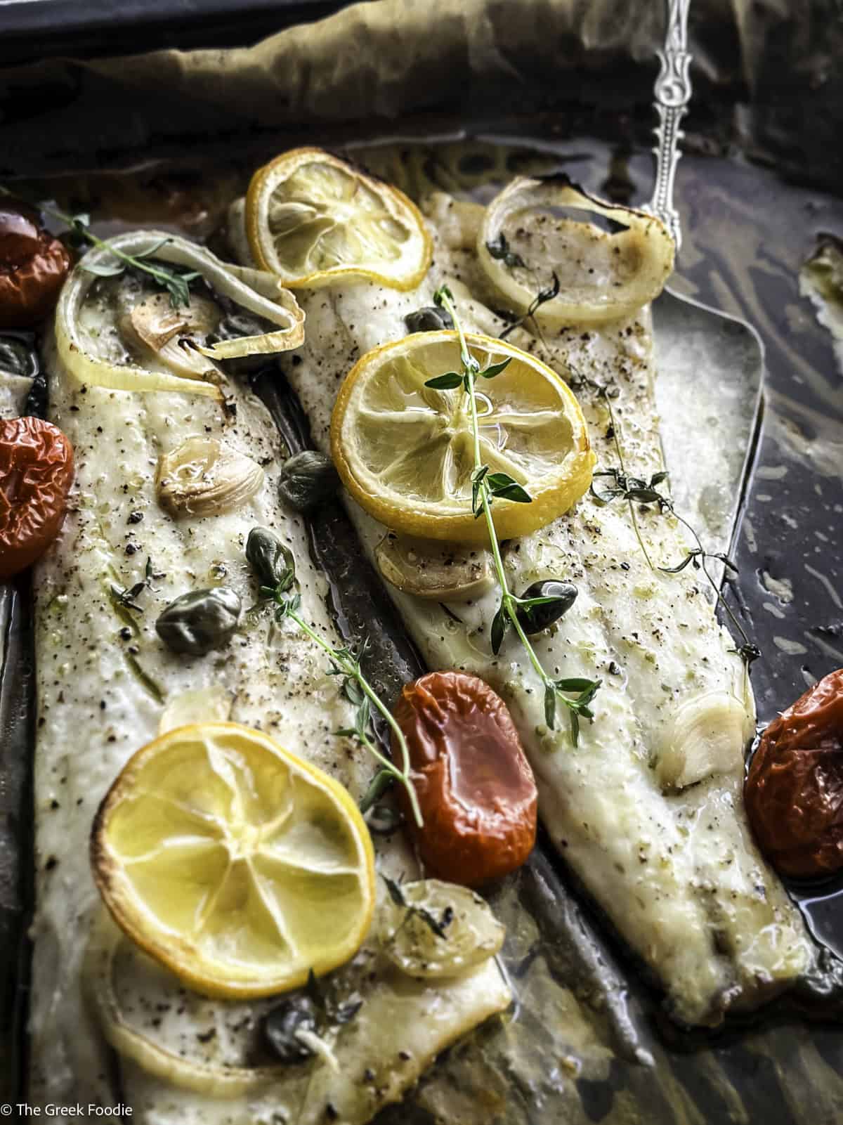 Roasted branzino fillets with cherry tomatoes and lemon slices in a baking tray.