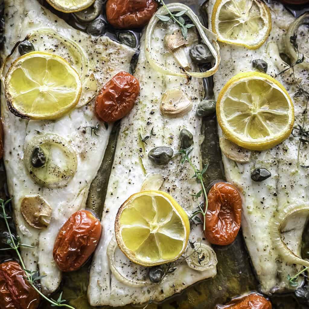 Roasted branzino fillets with cherry tomatoes and lemon slices in a baking tray.