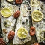 Roasted branzino fillets with cherry tomatoes and lemon slices in a baking tray.