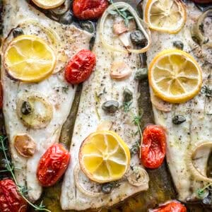 Roasted branzino fillets with cherry tomatoes and lemon slices in a baking tray.