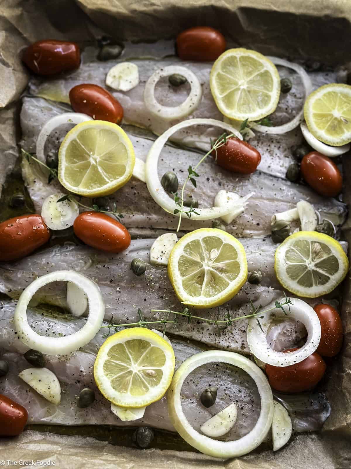 Branzino fillets with cherry tomatoes and lemon slices in a baking tray ready to be roasted.