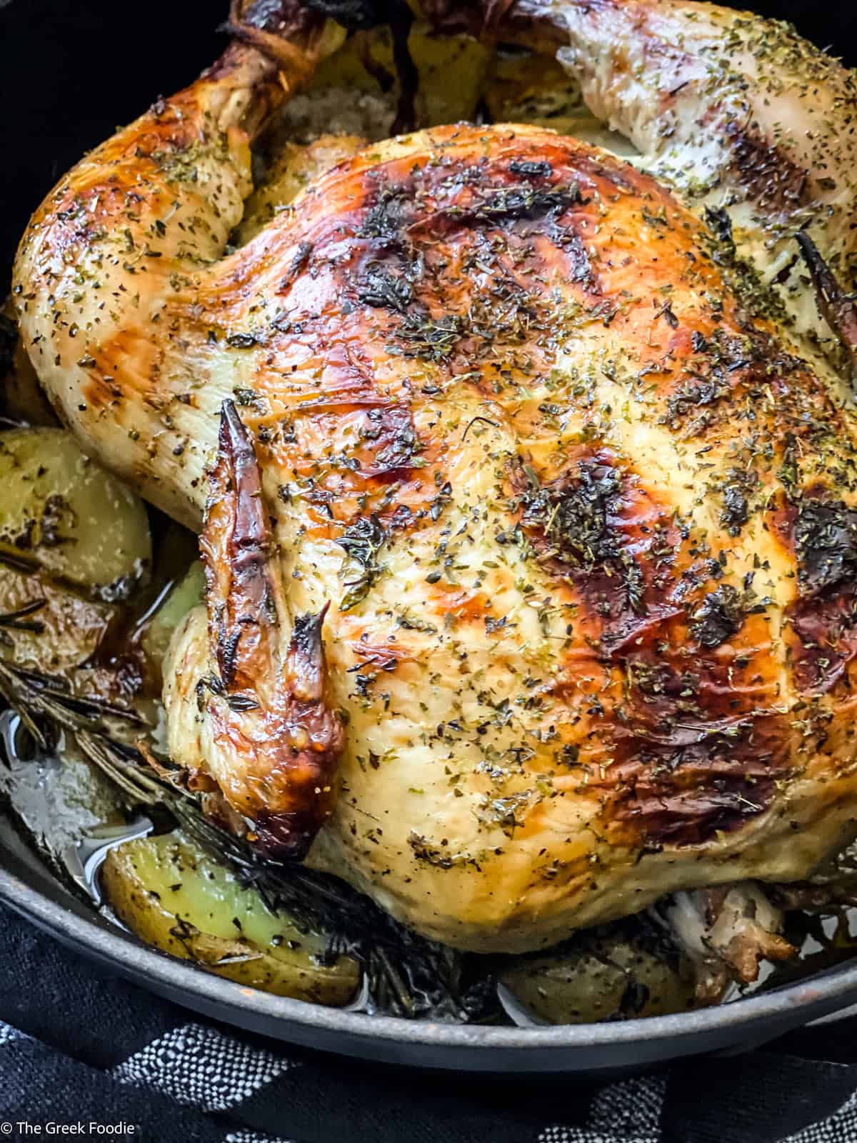 A chicken seasoned with fresh herbs in a black dutch oven.