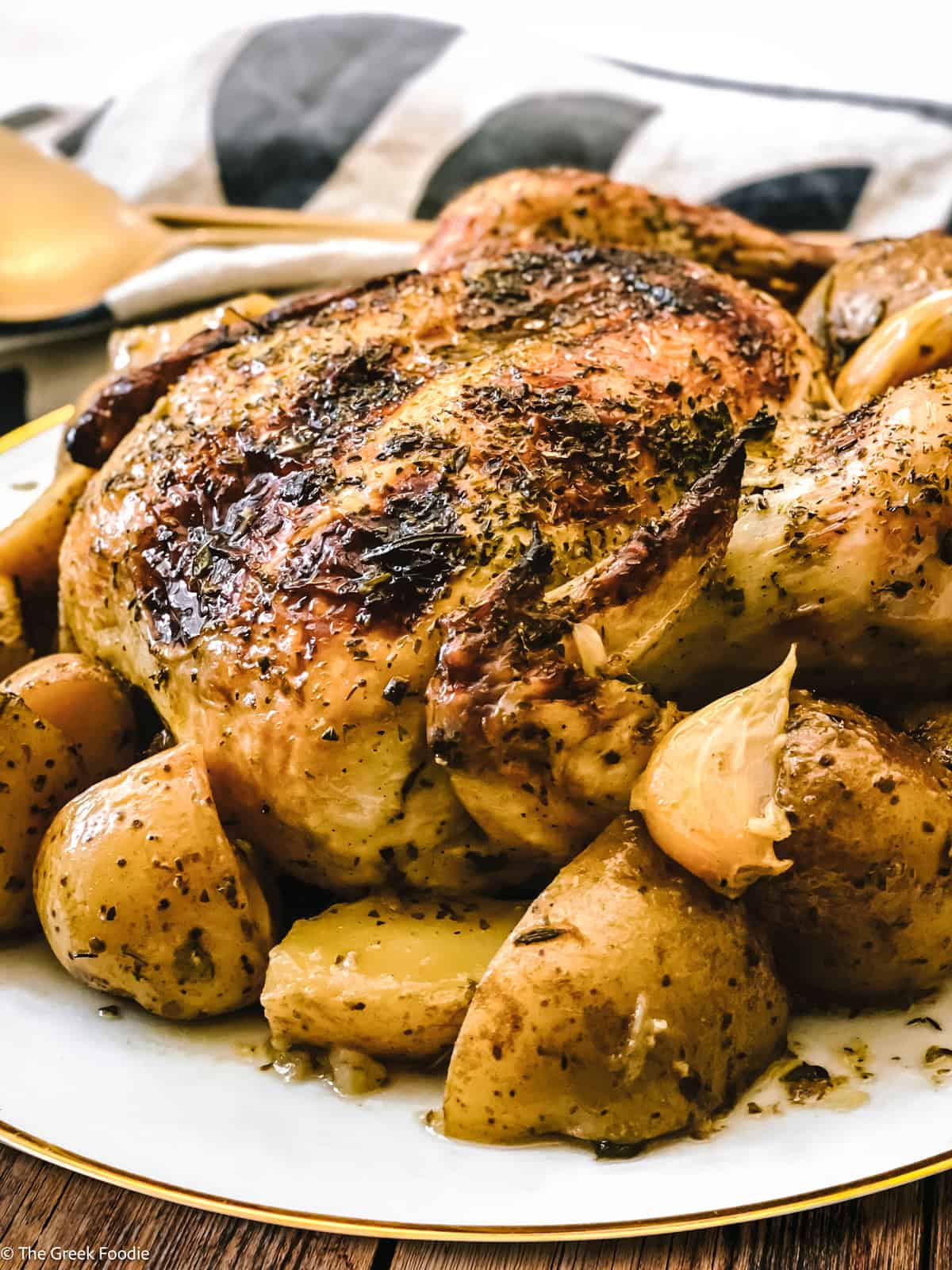 A roast chicken with potatoes on a platter with a cloth napkin and serving utensils.