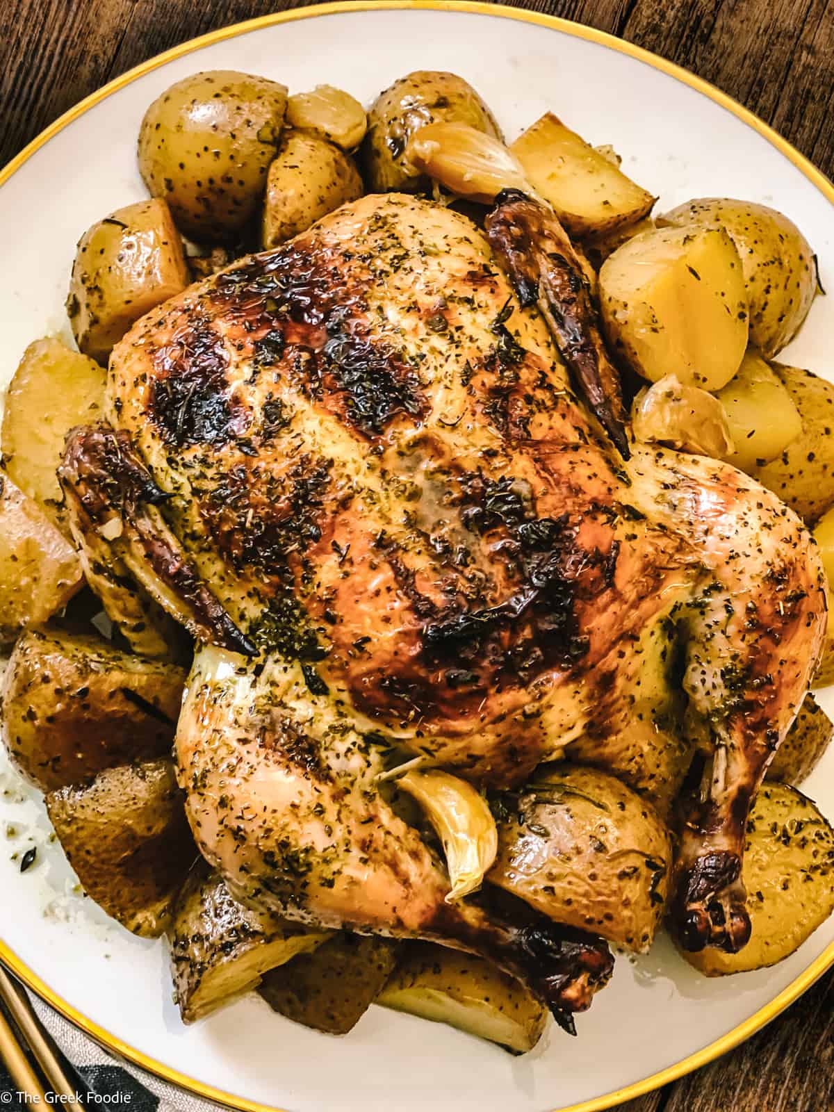 A roast chicken with potatoes on a platter with a cloth napkin and serving utensils.