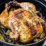 A chicken seasoned with fresh herbs in a black dutch oven.