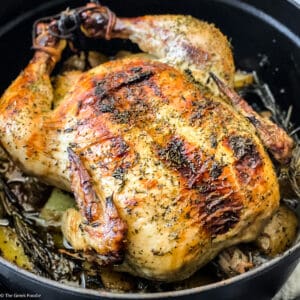 A chicken seasoned with fresh herbs in a black dutch oven.