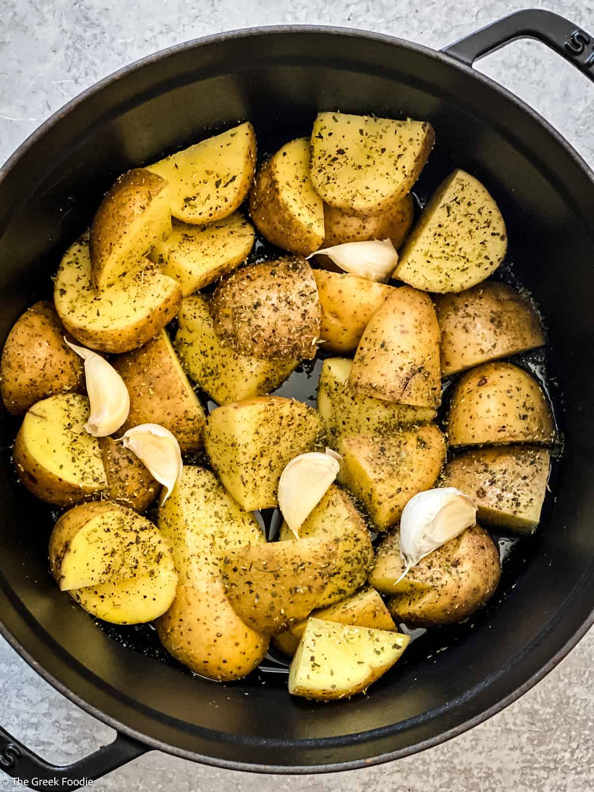 Potatoes and garlic and seasonings at the bottom of a dutch oven.