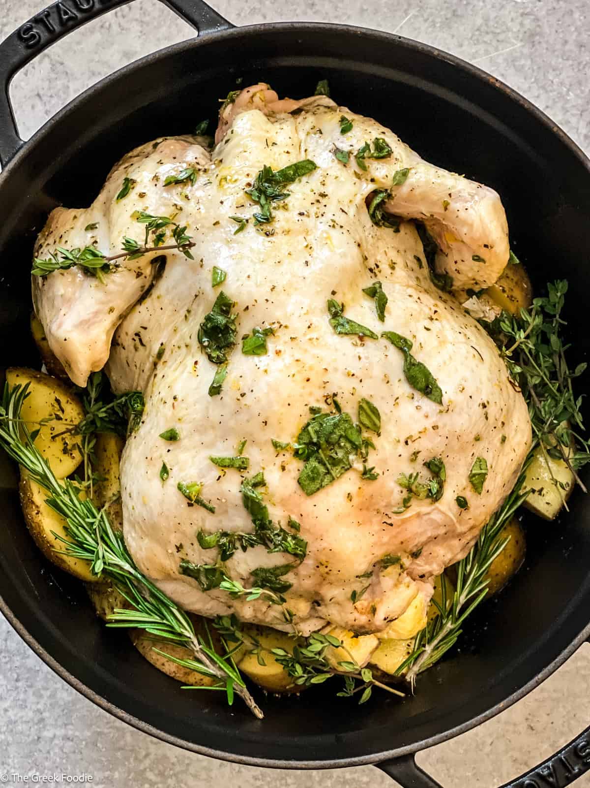 A chicken seasoned with fresh herbs in a black pot.