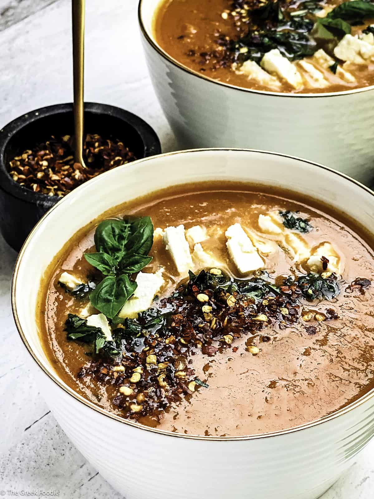 A bowl with Greek tomato soup with feta and basil, at the back another soup bowl.