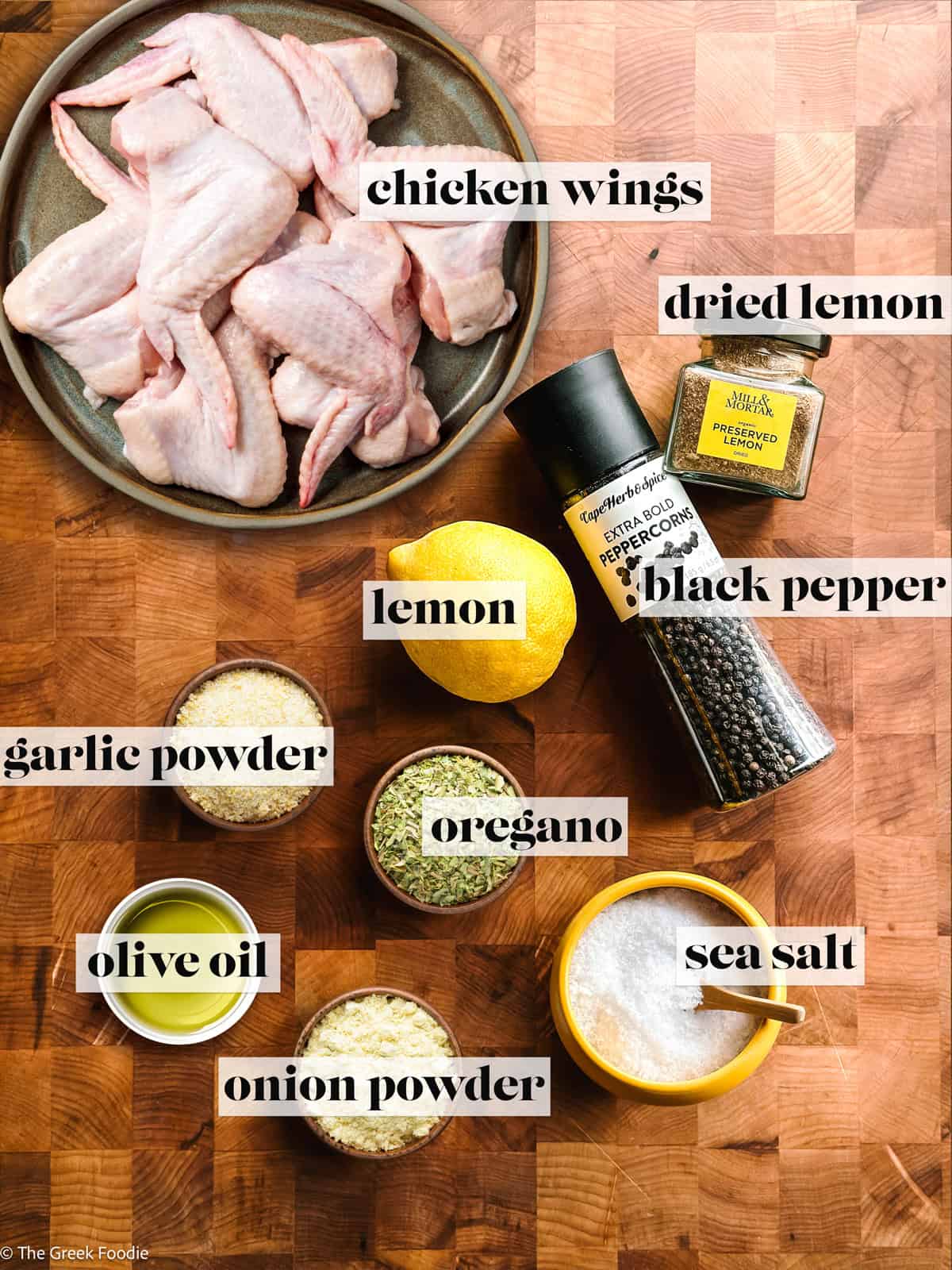 Chicken wings, lemon, dried lemon jar, pepper, salt, seasonings on a wooden surface for lemon pepper chicken wings.