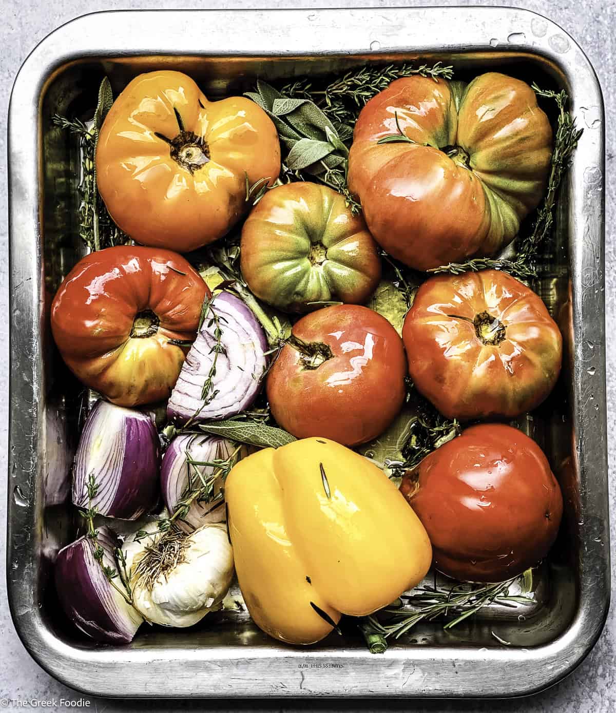 Tomatoes, onions garlic and bell pepper in a baking dish with fresh herbs.