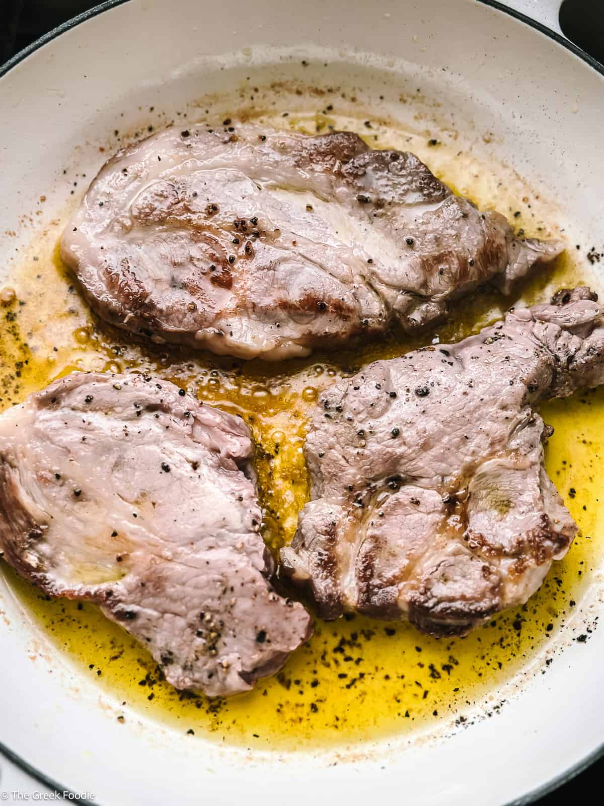 Pork shoulder pieces searing in olive oil in a pan.