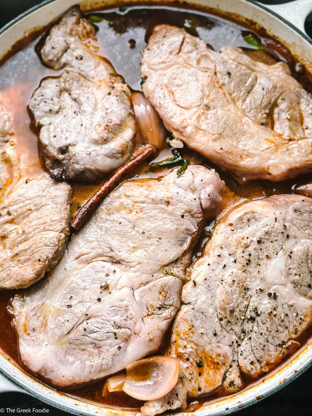 Pork shoulder pieces in sauce in a skillet.