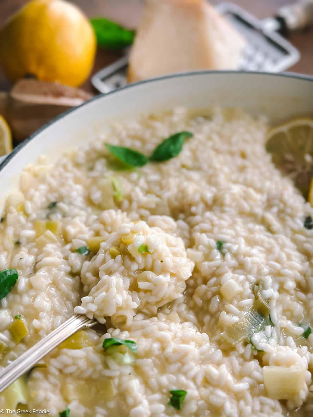 Creamy lemon herb risotto in a white large saucepan, a lemon, parmesan at the back.