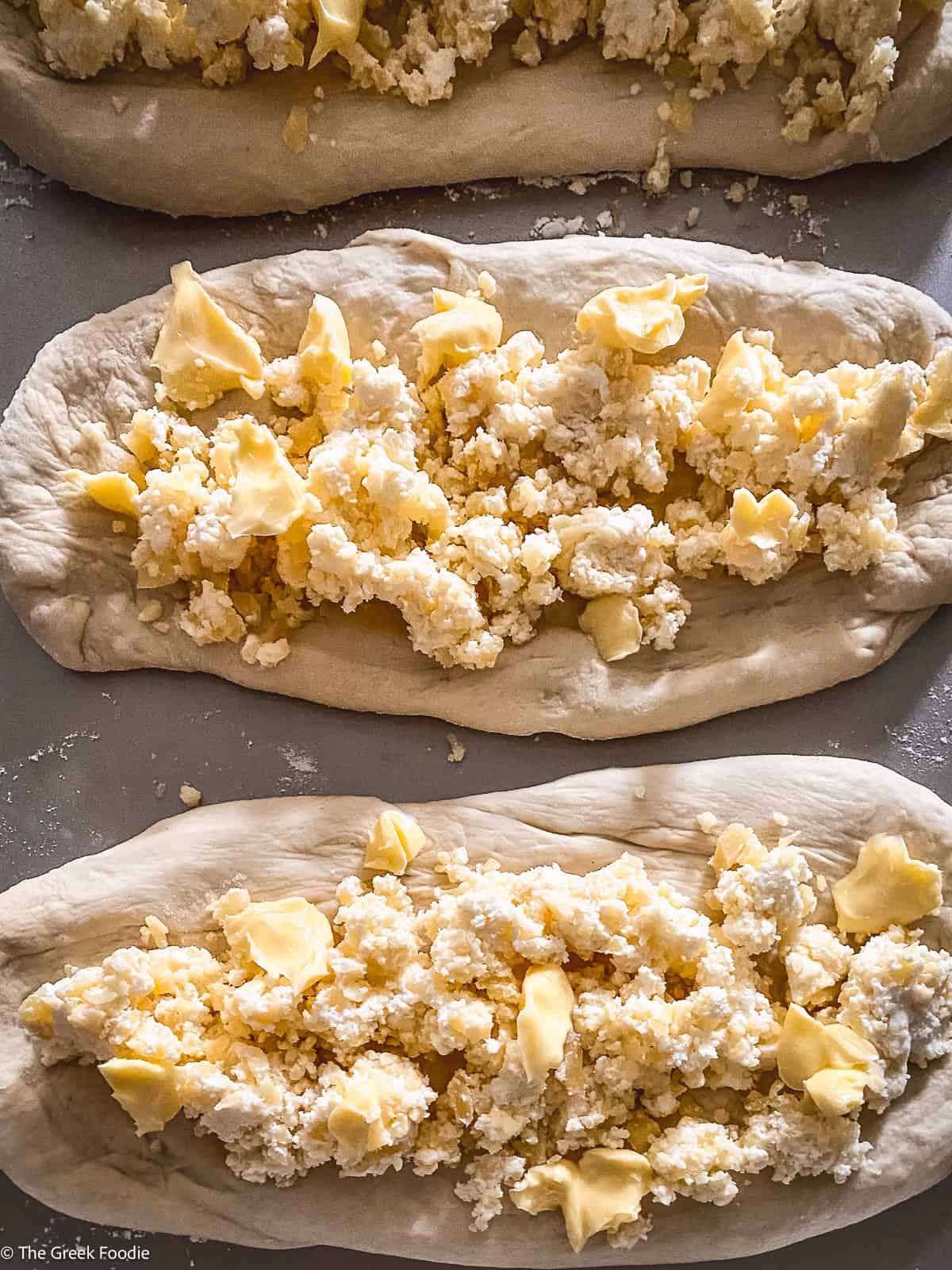 Three pieces of pizza dough elongated with cheese and cubes of butter on a baking sheet.