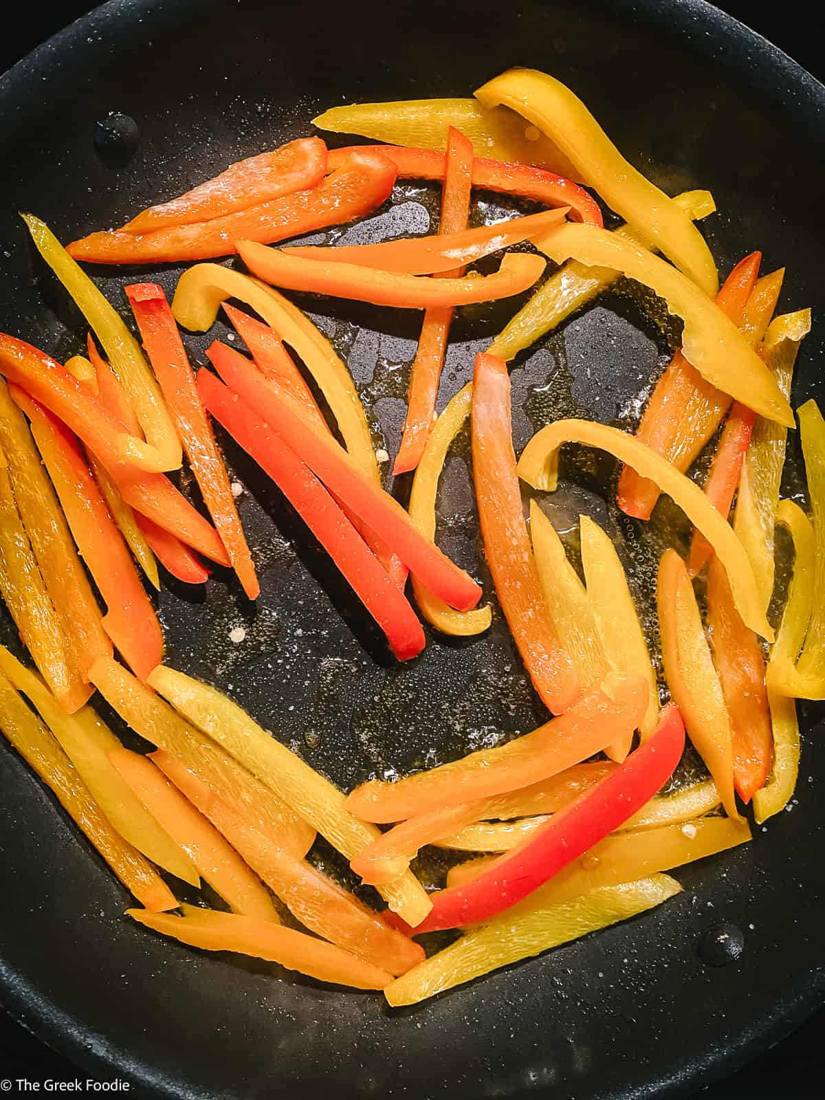 Sliced bell peppers with olive oil in a frying pan.