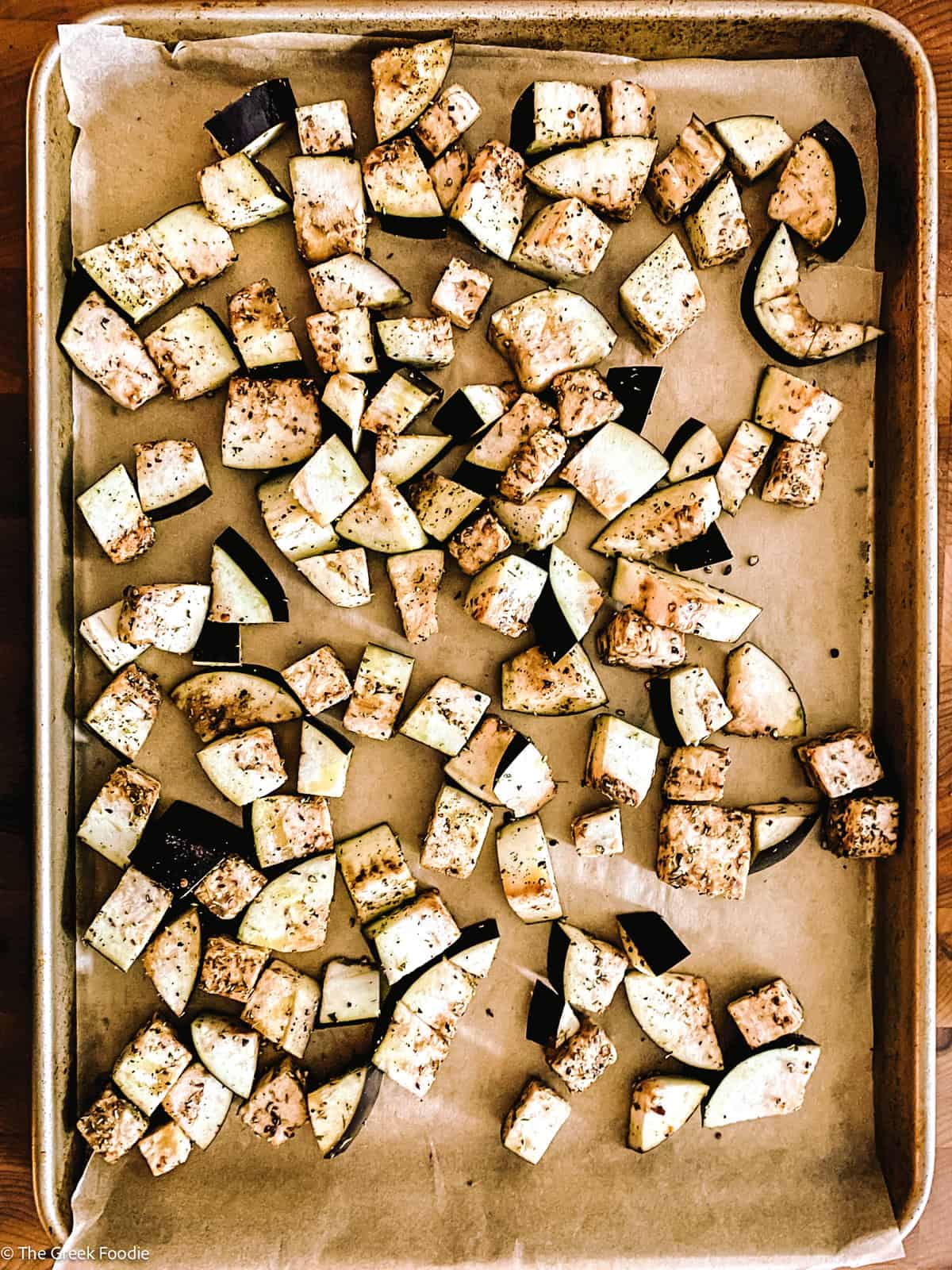 A baking sheet lined with parchment layered with eggplant cubes.